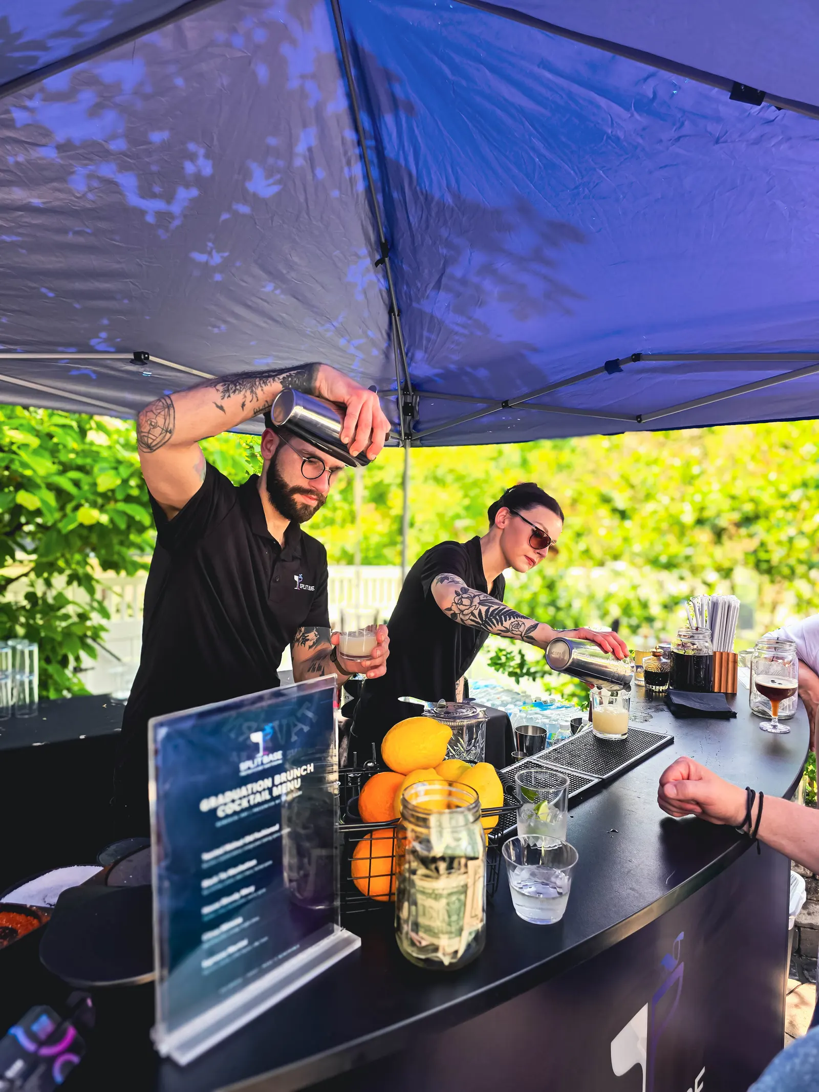 Two Split Base bartenders pouring drinks at a daytime event