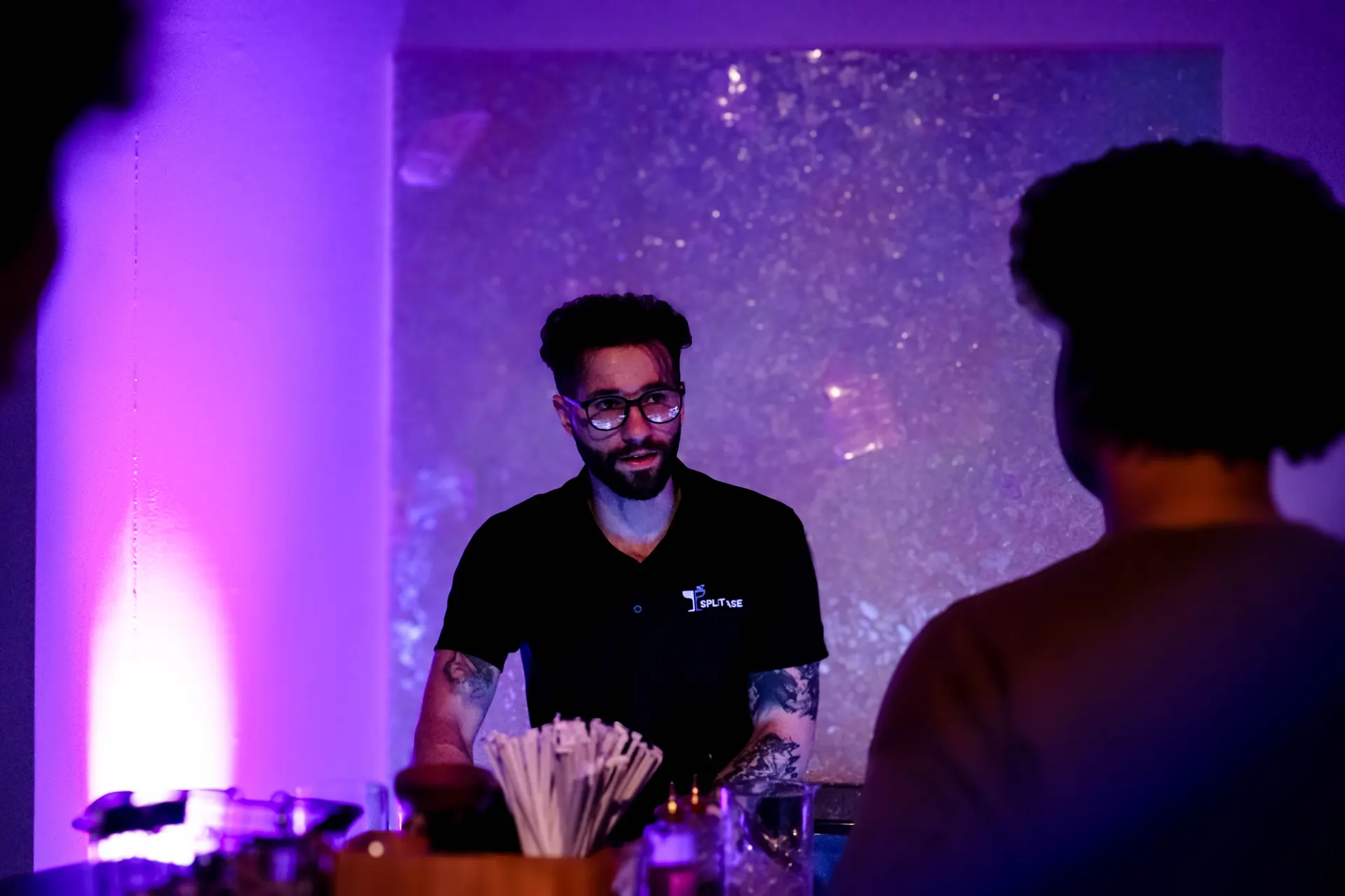 A Split Base bartender serving guests at the glowing bar